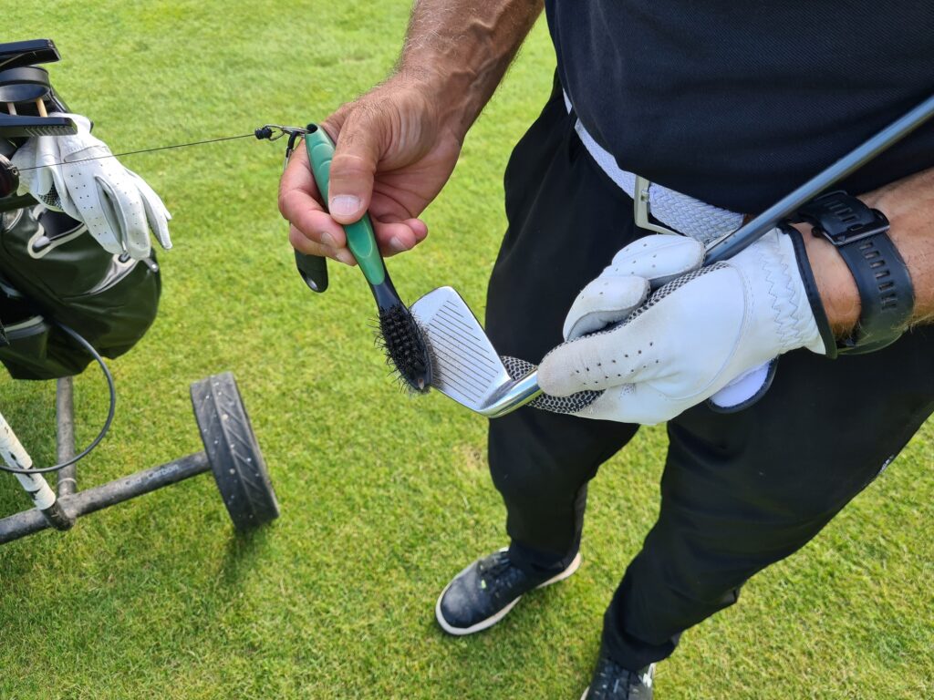 A male golfer cleans a golf club while on course. 