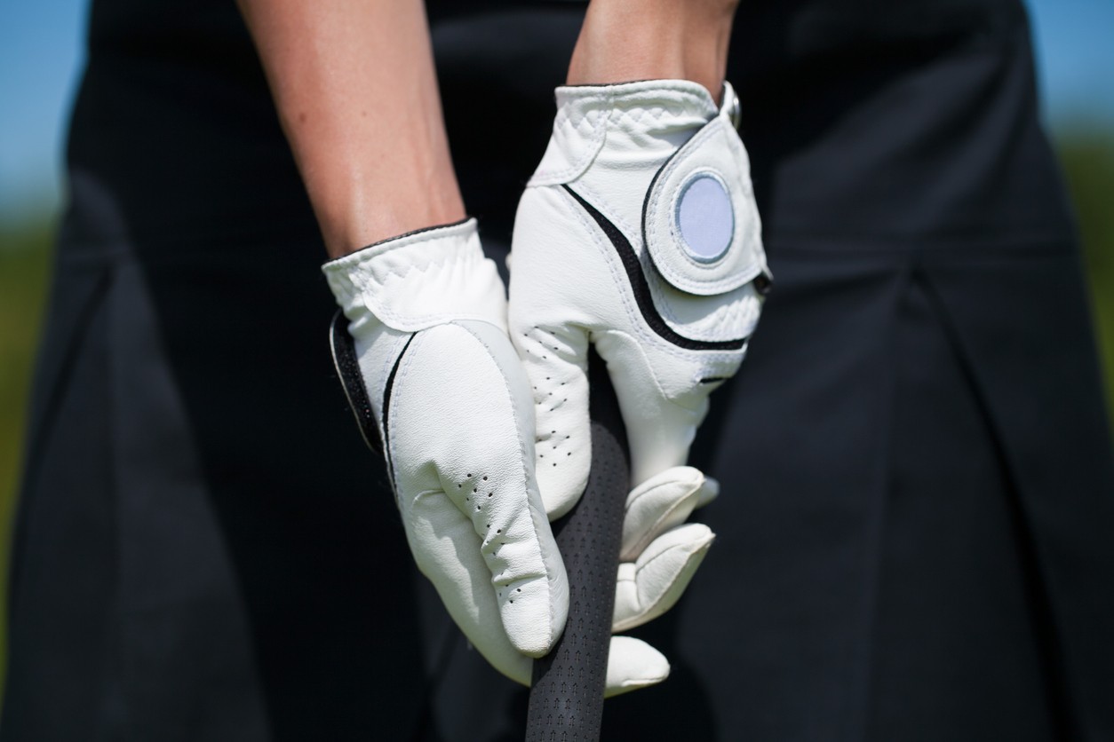 A close up of a female golfer with gloved hands holding a golf club and ready to tee off.