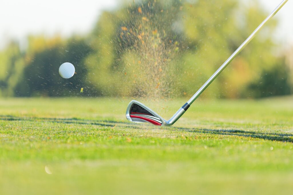 A close up of a golf wedge hitting a golf ball on the course. 