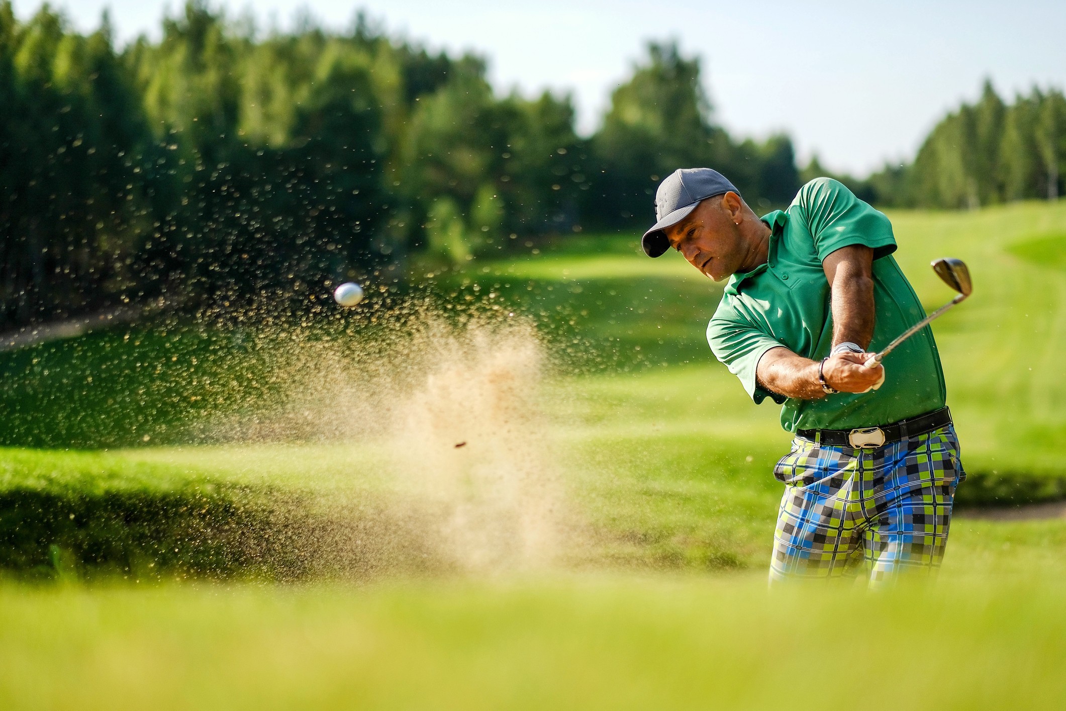 A golfer in a sand bunker chipping a shot out of the sand.