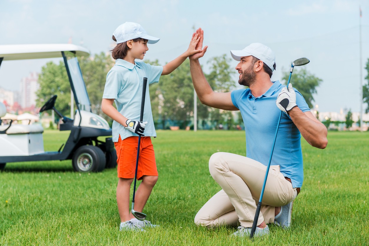 Father and son high five on a golf course. 