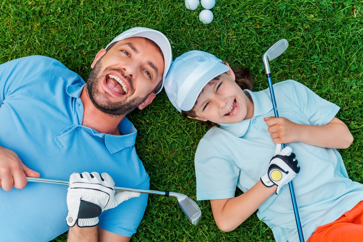 Father and son laying on a golf course smiling. 