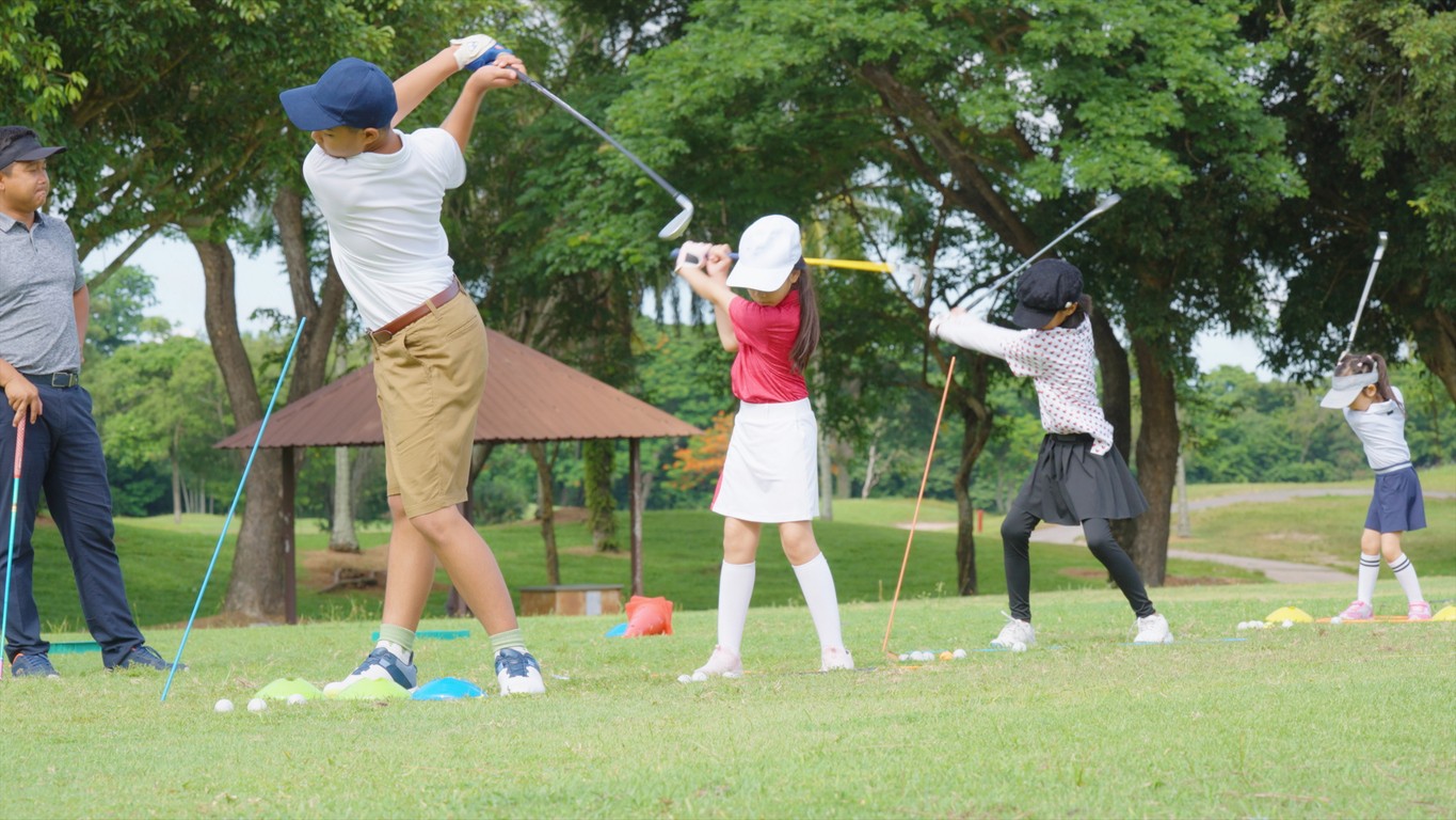 Kids swinging at golf balls on a range. 